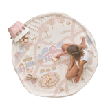 A child playing on a round playmat that features an illustrated ranch theme with trees, houses, and a road. Toys and a storage bag are also visible on the mat. Alt Img