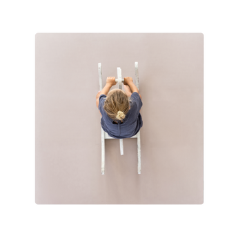 A person sitting on a blush-colored play mat with their hands raised. Alt Img