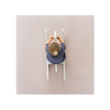 A person sitting on a blush-colored play mat with their hands raised. Alt Img