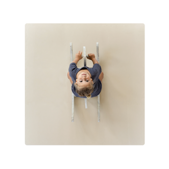 A baby lying on a beige play mat with a neutral expression. Alt Img