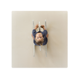 A baby lying on a beige play mat with a neutral expression. Alt Img