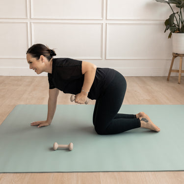 Woman exercising on a green Evo Mat with dumbbells in a home setting