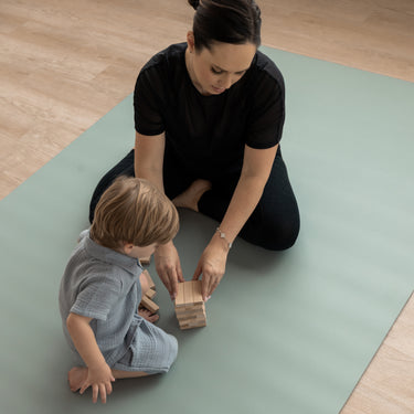 Woman and child playing with wooden blocks on a green Evo Mat