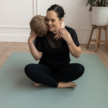 Woman and child sitting on a green Evo Mat indoors, embracing.