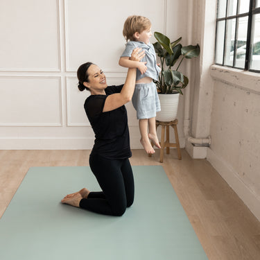 Woman lifting up a child on a green Evo Mat in a home setting