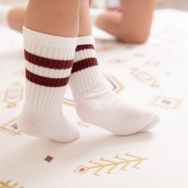 Close-up of baby toddler feet in striped socks standing on the toddlekind baby toddler foam modern designer puzzle play mat haven amira golden clay