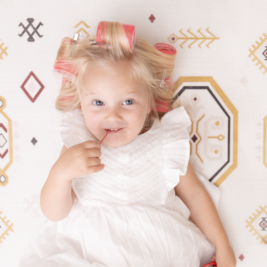 Baby toddler lying on the mat with hair rollers and holding a lollipop on the toddlekind baby toddler foam modern designer puzzle play mat haven amira golden clay.