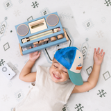 Overhead view of baby toddler lying down with a toy radio, enjoying the toddlekind baby toddler foam modern designer puzzle play mat haven amira seagrass