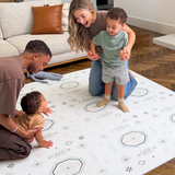 Family interacting with baby toddler on the floor in a cozy living room, highlighting the toddlekind baby toddler foam modern designer puzzle play mat haven amira seagrass.