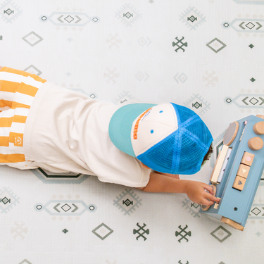 Baby toddler lying on stomach playing with a toy on the toddlekind baby toddler foam modern designer puzzle play mat haven amira seagrass.
