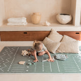 Toddler kneeling and playing with toys on toddlekind baby toddler foam modern designer puzzle play mat haven berber moss with pillows and wooden accents.