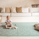 Baby sitting and playing with toys on toddlekind baby toddler foam modern designer puzzle play mat haven berber moss in a neutral living room.