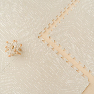 Wooden toy car placed on the toddlekind baby toddler foam modern designer puzzle play mat haven deco ecru showing subtle pattern detail.