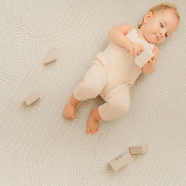 Baby lying on back playing with wooden blocks on toddlekind baby toddler foam modern designer puzzle play mat haven deco ecru.
