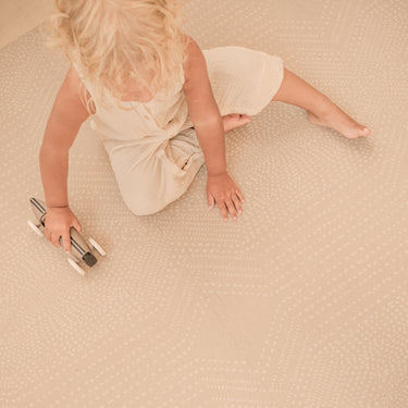 Toddler sitting and playing with a toy car on the toddlekind baby toddler foam modern designer puzzle play mat haven deco latte.