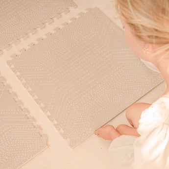 Person assembling interlocking tiles of the toddlekind baby toddler foam modern designer puzzle play mat haven deco latte on a light floor.