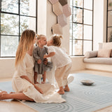 Mother sitting while toddler kisses baby on the cheek on the toddlekind baby toddler foam modern designer puzzle play mat haven linear mineral.