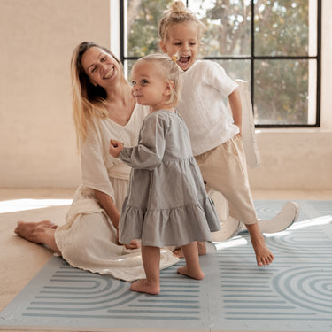 Smiling mother with baby and toddler playing together on the toddlekind baby toddler foam modern designer puzzle play mat haven linear mineral.