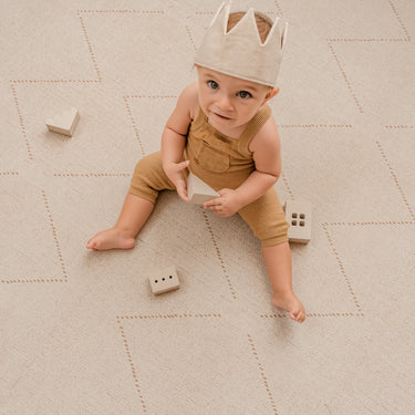 Baby sitting and looking up while holding a toy block on the toddlekind baby toddler foam modern designer puzzle play mat haven tulum bone.