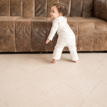 Toddler walking near a sofa on the toddlekind baby toddler foam modern designer puzzle play mat haven tulum bone.
