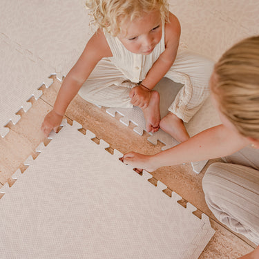 Toddler and caregiver assembling tiles together on toddlekind baby toddler foam modern designer puzzle play mat haven wild dune.