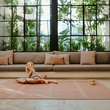Wide living room scene with toddler lounging on pillows on the toddlekind baby toddler foam modern designer puzzle play mat haven linear camel.