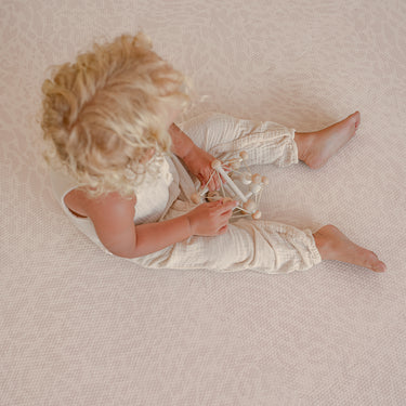 Toddler sitting and playing with wooden toy on toddlekind baby toddler foam modern designer puzzle play mat haven wild dune.