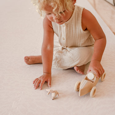 Toddler pushing wooden toy car across toddlekind baby toddler foam modern designer puzzle play mat haven wild dune.