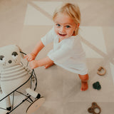 Baby standing and smiling while holding toy stroller on toddlekind baby toddler foam modern designer puzzle play mat haven kyte mocha