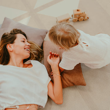 Mother lying on cushions interacting with toddler on toddlekind baby toddler foam modern designer puzzle play mat haven kyte mocha.
