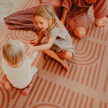 Mother and toddler sitting together and playing on the toddlekind baby toddler foam modern designer puzzle play mat haven linear camel.