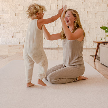 Mother and toddler playing together and high-fiving on toddlekind baby toddler foam modern designer puzzle play mat haven wild dune.