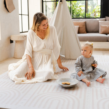 Mother and baby toddler sitting together indoors with cookies on the toddlekind baby toddler foam modern designer puzzle play mat haven linear linen.