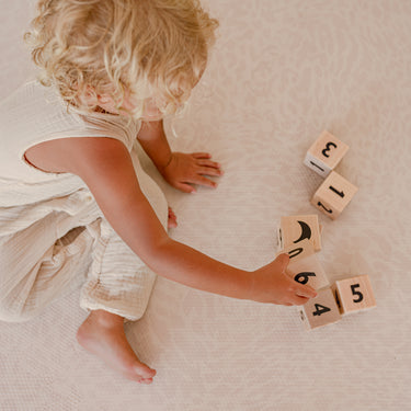 Toddler playing with wooden number blocks on toddlekind baby toddler foam modern designer puzzle play mat haven wild dune
