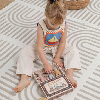 A child sits on the Toddlekind Haven Playmat in Linear Putty, playing with a soft toy. The cushioned foam play mat features a modern geometric pattern, creating a comfortable and stylish space for everyday play.