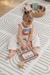 A child sits on the Toddlekind Haven Playmat in Linear Putty, playing with a soft toy. The cushioned foam play mat features a modern geometric pattern, creating a comfortable and stylish space for everyday play.