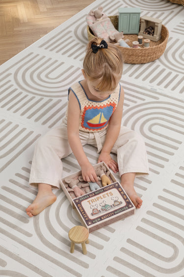 A child sits on the Toddlekind Haven Playmat in Linear Putty, playing with a soft toy. The cushioned foam play mat features a modern geometric pattern, creating a comfortable and stylish space for everyday play.