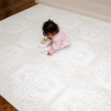 1. Overhead view of toddler sitting on a large assembled mat, highlighting full coverage of the toddlekind baby toddler foam modern designer puzzle play mat haven parisa millet.