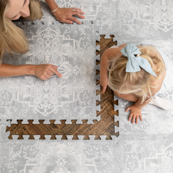 Mother and toddler assembling foam tiles on a wooden floor, demonstrating easy setup of the toddlekind baby toddler foam modern designer puzzle play mat haven parisa pearl blue.