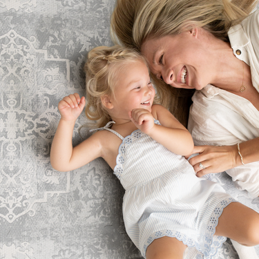 Mother and child lying together smiling on the mat, capturing bonding moments on the toddlekind baby toddler foam modern designer puzzle play mat haven parisa pearl blue.