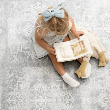 Child reading a book with a plush toy on the foam mat, highlighting quiet time on the toddlekind baby toddler foam modern designer puzzle play mat haven parisa pearl blue.